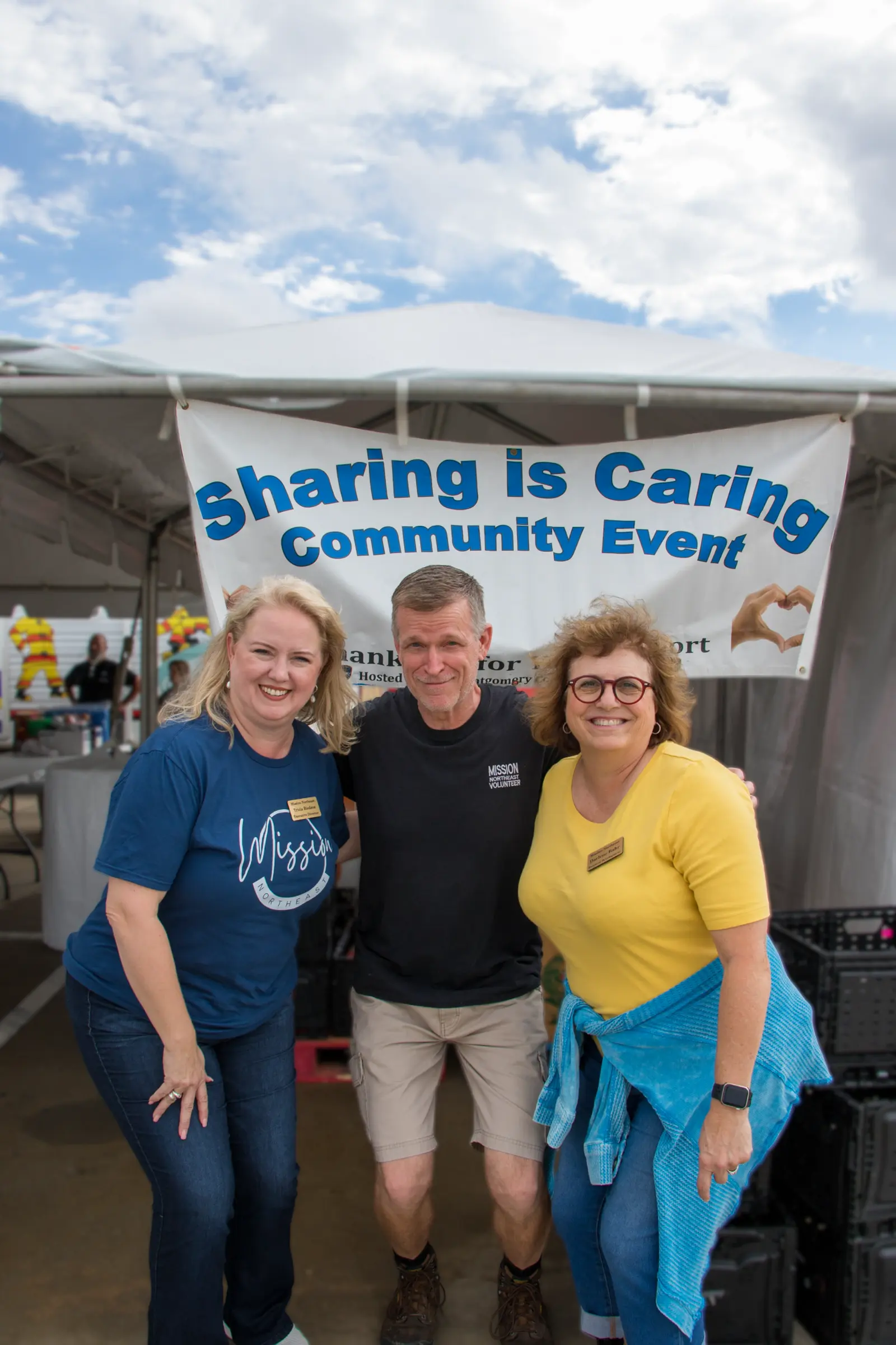 Three volunteers under the Sharing is Caring banner.