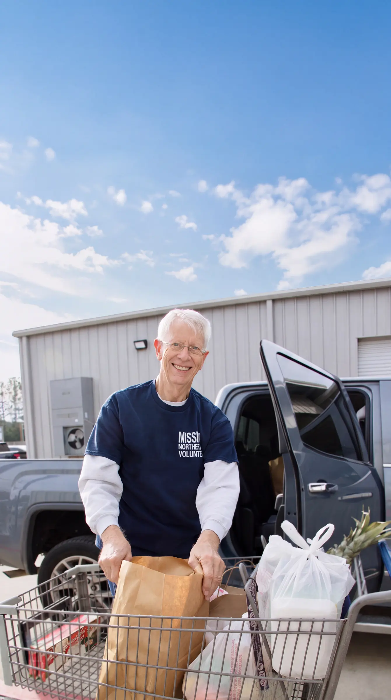 A volunteer loads grocery bags from a cart into a pickup outside the warehouse.
